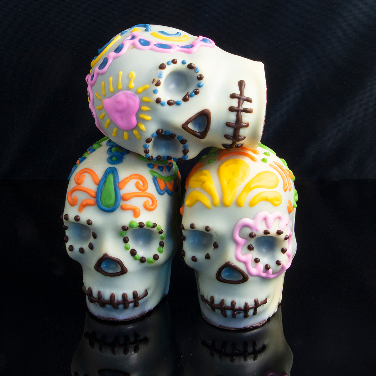 Three colorful sugar skulls stacked on black surface.