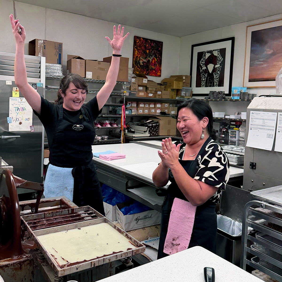 Two women joyfully celebrating in a bakery kitchen.