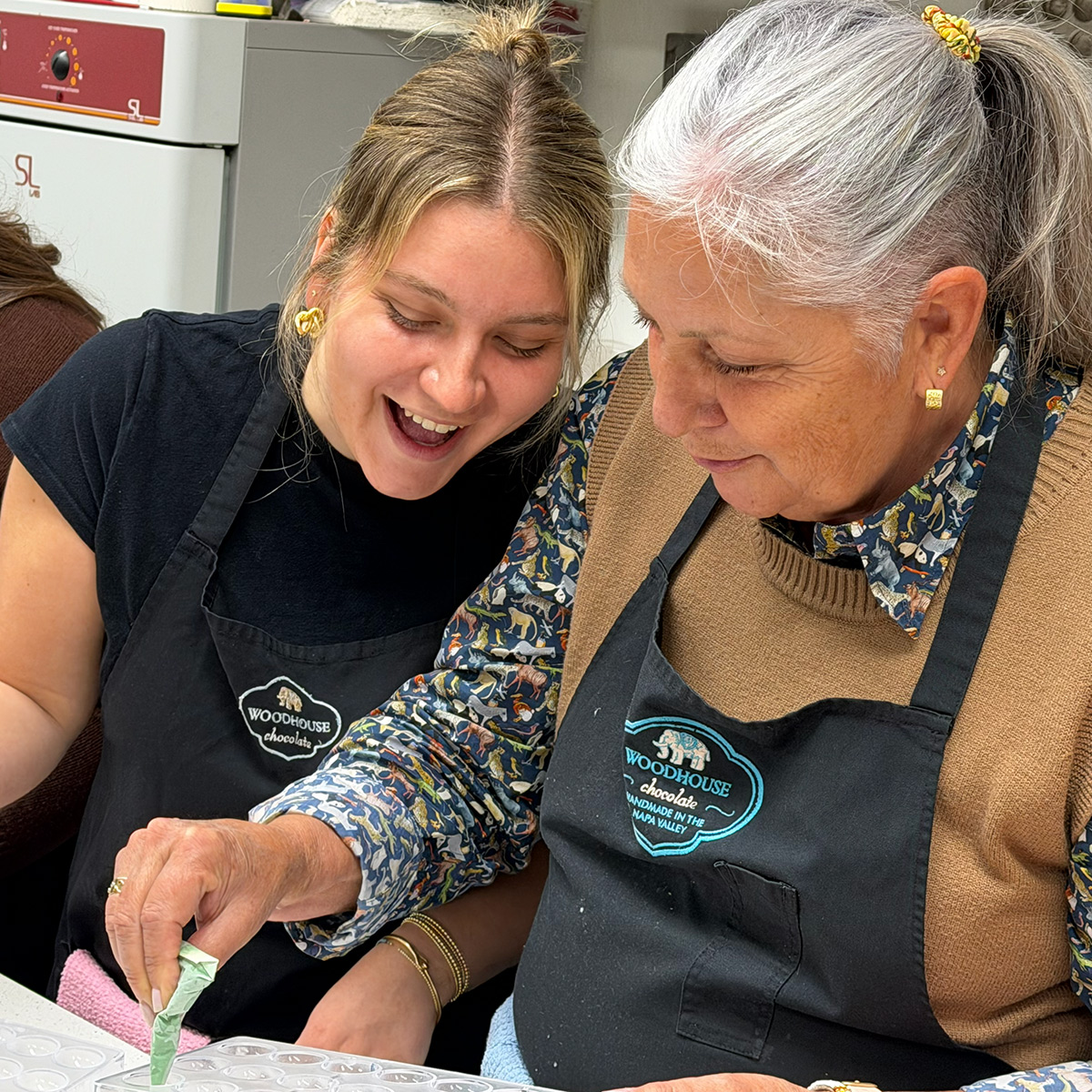 A young woman helps an elderly woman with a craft activity, both smiling.