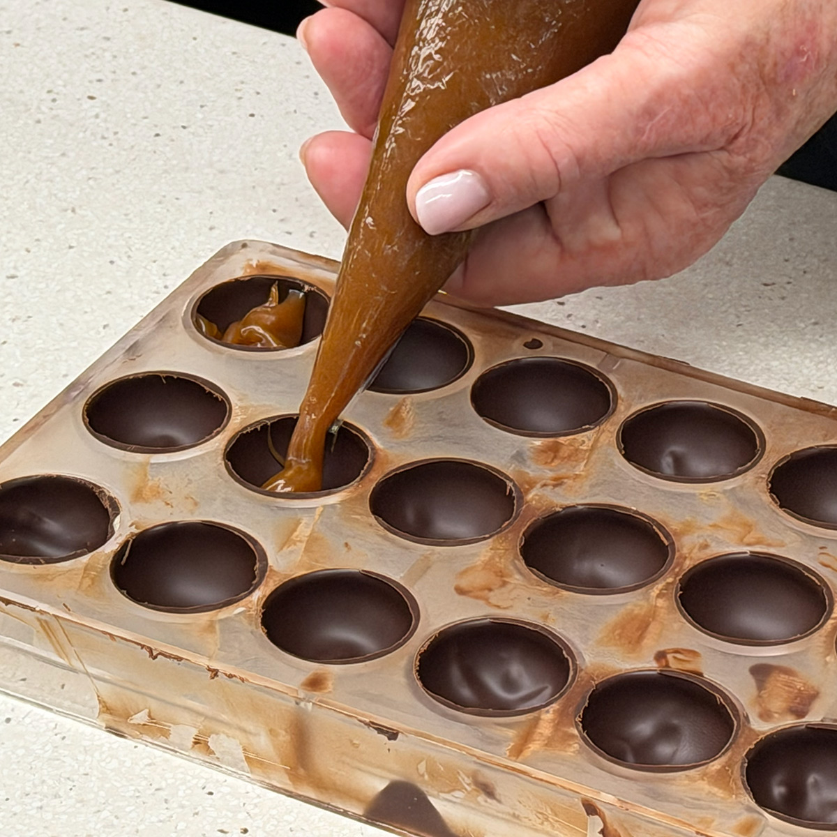 Hand filling chocolate molds with melted chocolate using a piping tool.
