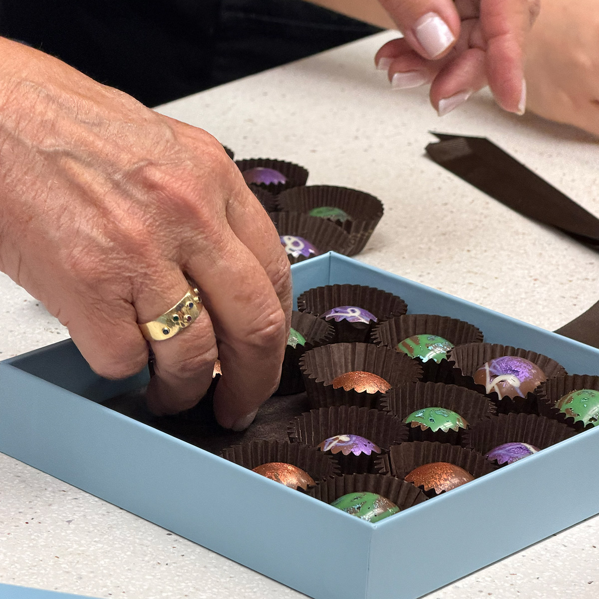 Hand picking a colorful chocolate from a box of assorted chocolates.